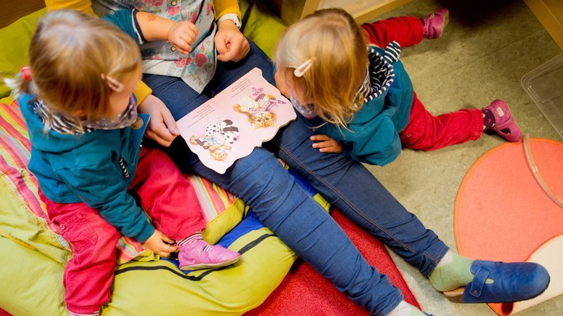 Eine Erzieherin liest mit Zwillingen ein Buch in einer Kindertagesstätte der Arbeiterwohlfahrt (AWO). © Julian Stratenschulte/dpa