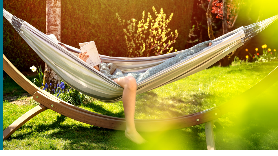 Person liest in einer Hängematte im Garten. Sonnenlicht filtert durch Blätter und erzeugt Lichtmuster.