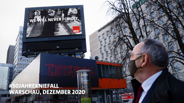 Norbert Walter-Borjans im Dezember 2020 in Warschau. Er schaut sich auf einer öffentlichen Leinwand die Szenen von Willy Brandts Kniefall 1970 an.
