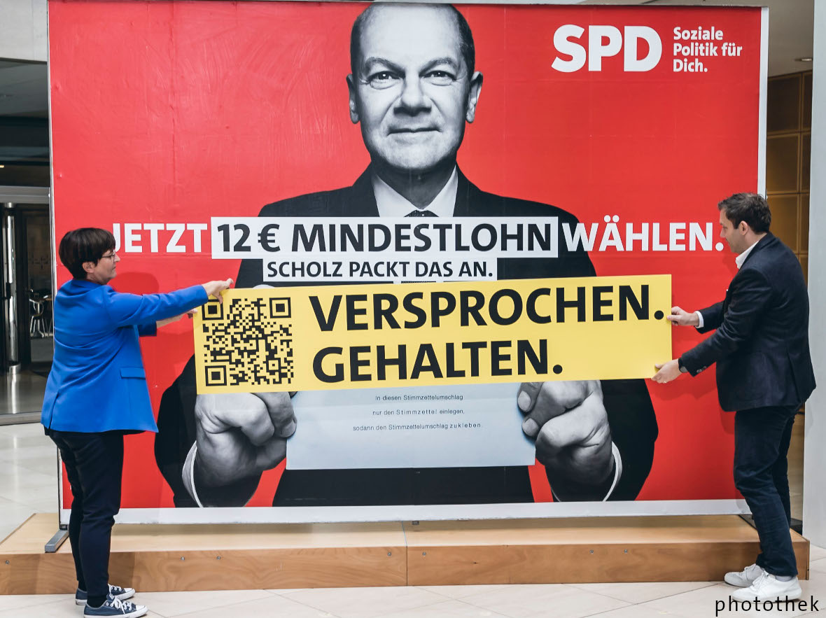 Saskia Esken und Lars Klingbeil bei der Pressekonferenz, nachdem der Mindestlohn beschlossen wurde. Im Hintergrund ist das Wahlplakat mit der Aufschrift "Jetzt 12 € Mindestlohn wählen. Scholz packt das an." Unsere Parteivorsitzenden bringen einen Störer an. Aufschrift: "Versprochen. Gehalten." Foto: Photothek.