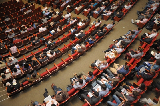 (2) People sitting in rows at a conference in a lecture hall